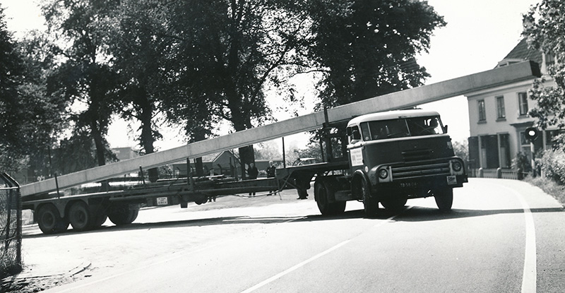 Zwart-witfoto van en vrachtwagen die door het dorp rijdt